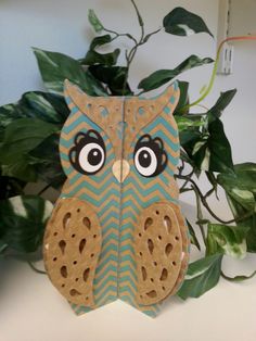 an owl made out of cardboard sitting next to a potted plant