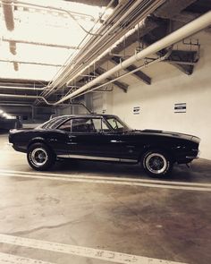 an old black car is parked in a parking garage with no one around it,