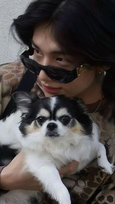 a woman holding a small black and white dog in her arms with sunglasses on it's face