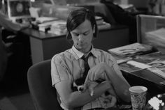a man sitting at a desk with a cat in his lap while holding the kitten