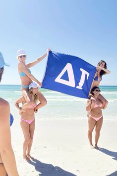 a group of young women standing on top of a sandy beach next to the ocean