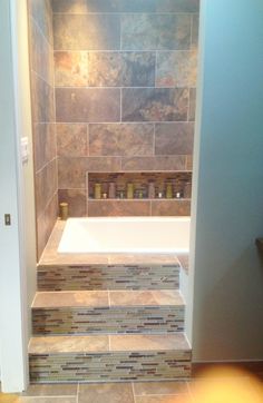 a bath tub sitting under a window next to a tiled wall in a home bathroom