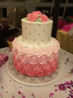 a three tiered cake with pink and white frosting roses on it sitting on a table