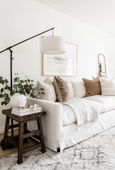 a living room with white couches and pillows on top of the sofa, next to a coffee table