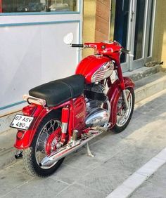 a red motorcycle parked on the side of a street next to a building with windows