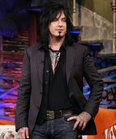 a man with black hair and piercings standing in front of an orange couch wearing a suit