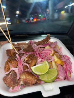 a white plate topped with meat and onions next to a green slice of lime wedge