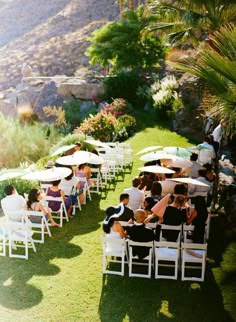 a group of people sitting on lawn chairs under umbrellas in the grass next to mountains