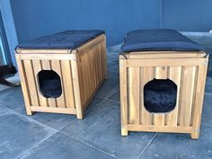 two wooden dog houses with black cushions on the floor and one has a cat in it