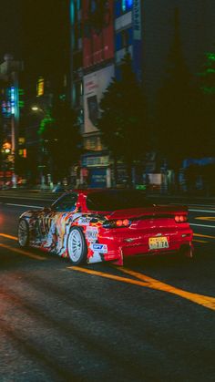 a red car driving down a street at night