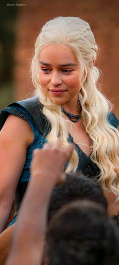 a woman with long blonde hair wearing a black dress and holding her hand up to the side