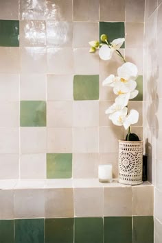 a vase with flowers in it sitting on a shelf next to a bath tub and tiled wall