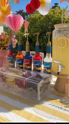 a table topped with lots of bottles of liquid next to a vase filled with flowers