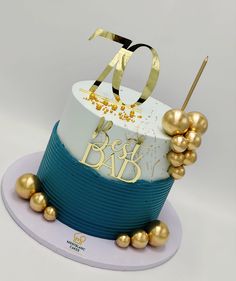 a white and blue cake with gold decorations on it's top that reads 70 best dad