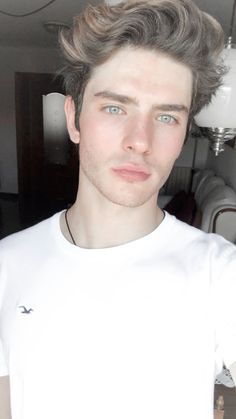 a young man with grey hair wearing a white t - shirt and looking at the camera