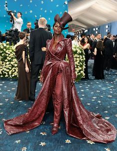 a woman in a red gown and hat standing on a blue carpet