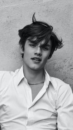 black and white photograph of a young man with his hair blowing in the wind, leaning against a wall