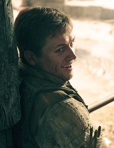 a man leaning against a tree with his hand on the back of his shoulder and looking off into the distance