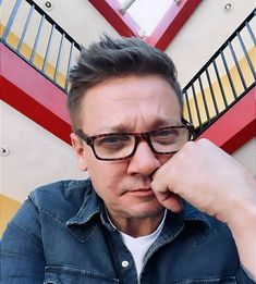 a man with glasses is looking at the camera and has his hand on his chin