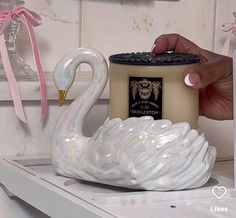 a white swan shaped candle holder sitting on top of a shelf next to a can