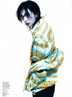 a woman with black hair wearing a blue and yellow shirt is standing in front of a white background