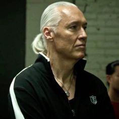 an older man with white hair and wearing a black hoodie looks off into the distance