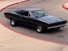 an old muscle car is parked on the street in front of a parking lot with no one around it
