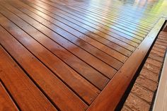a close up of a wooden deck with water on the ground and trees in the background