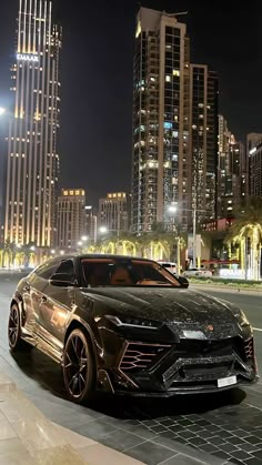 a black sports car is parked in front of some tall buildings at night with its lights on