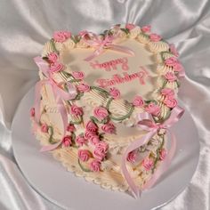a heart shaped cake decorated with pink roses and ribbons on a white tableclothed surface
