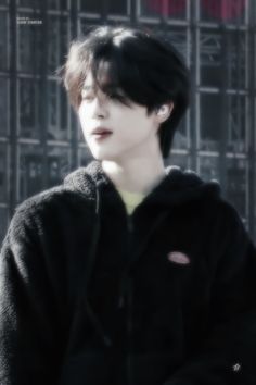 a young man with black hair wearing a hoodie and standing in front of a building