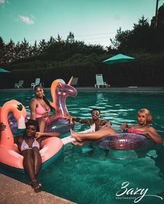 four women sitting on inflatable flamingos at the edge of a swimming pool