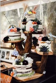 a table topped with three tiered cakes covered in frosting and colorful flowers on top of wooden slices