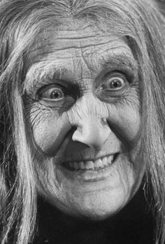 an old woman with long hair and big eyes smiles at the camera in this black and white photo