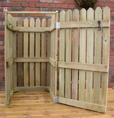 an open wooden gate sitting on top of a hard wood floor next to a brick wall