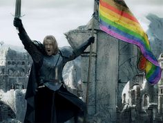 a woman holding a rainbow flag in front of an old castle with mountains behind her