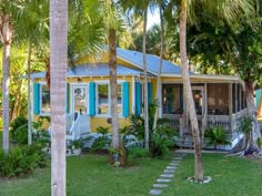 a small yellow house with blue shutters and palm trees in the front yard area