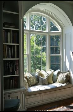 a window seat with pillows on it in front of a bookshelf filled with books
