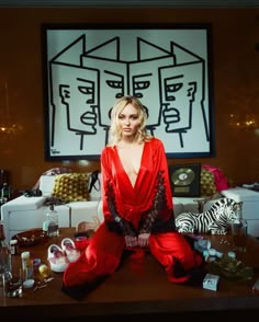 a woman sitting on top of a wooden table in front of a wall with art