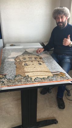 a man sitting at a table with a painting on it's surface in front of him