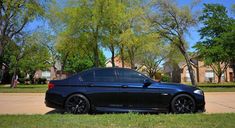 a black car parked on the side of a road in front of trees and houses