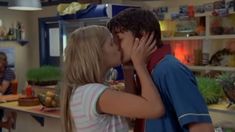 a young man and woman kissing each other in front of a table with food on it