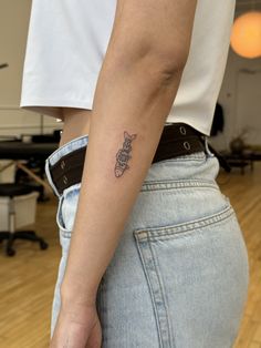 a person with a small tattoo on their left arm, wearing jeans and a white t - shirt