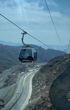 a cable car going up the side of a mountain with a road below it and mountains in the background