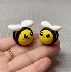 two tiny yellow and black bee earrings on someone's hand