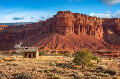 an old cabin sits in the desert with mountains in the backgrouds and clouds in the sky