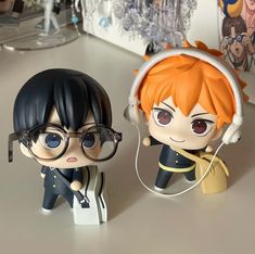 two anime figurines sitting on top of a table next to each other with headphones