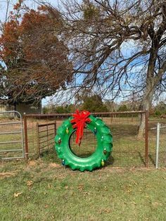an inflatable wreath sits on the grass next to a fence with a red bow