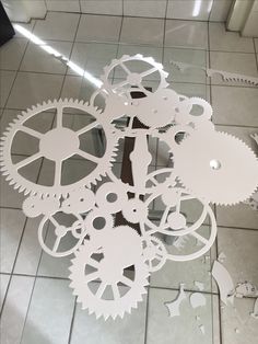 a clock made out of white gears on a tile floor in front of a mirror