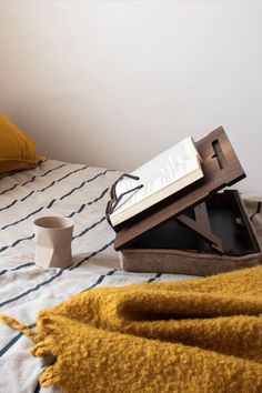 an open book sitting on top of a bed next to a cup and saucer